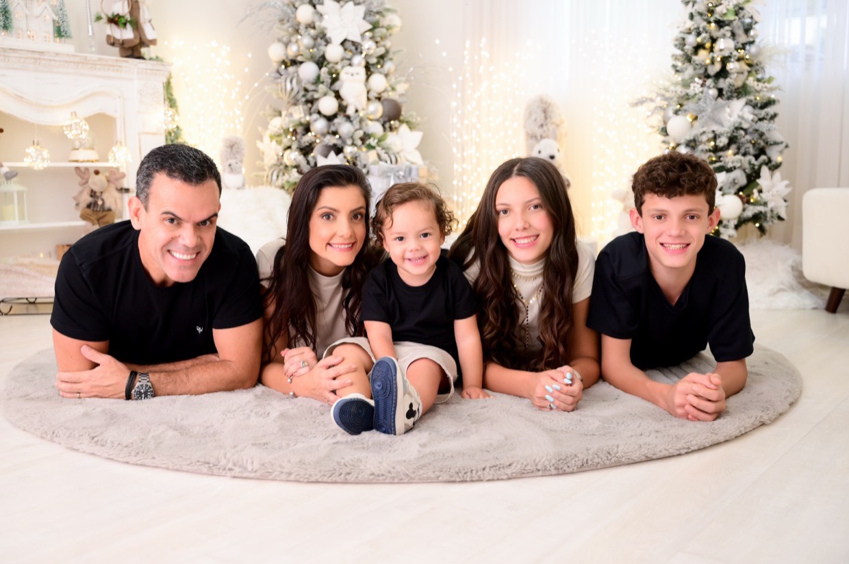Os cinco da família deitados lado a lado sobre um tapete claro, em um estúdio de fotografia.