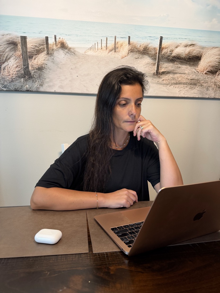 Drica Ricci sentada diante de um notebook, com a mão apoiada no rosto, concentrada.